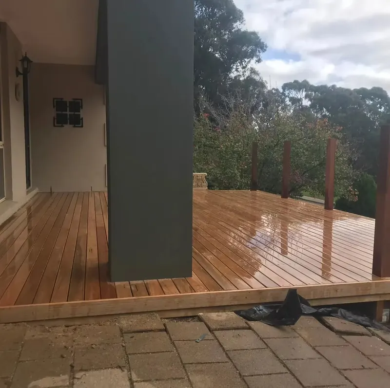 Freshly oiled timber deck wrapping a dark wall, with gum trees beyond