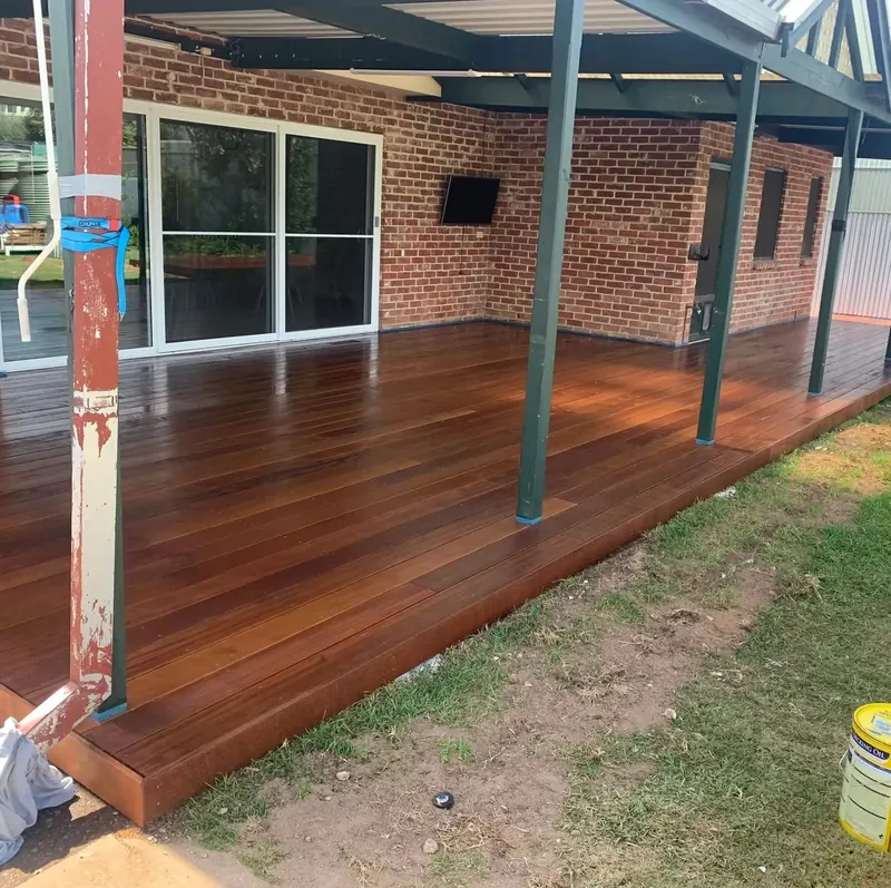Covered timber deck with dark steel posts beside a brick home