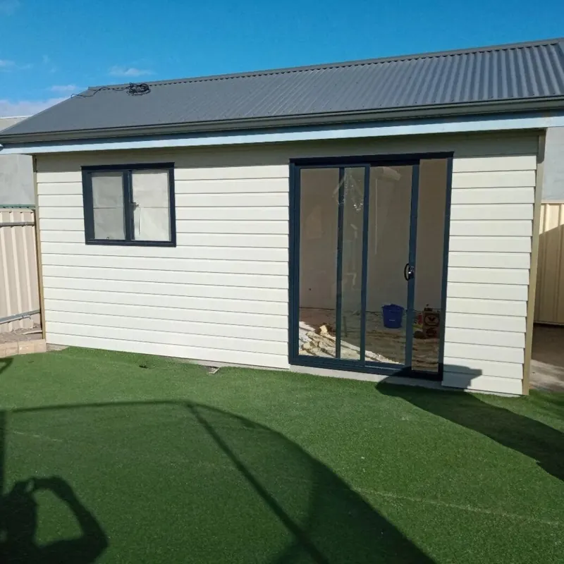 Clad backyard studio with sliding glass doors on a synthetic lawn