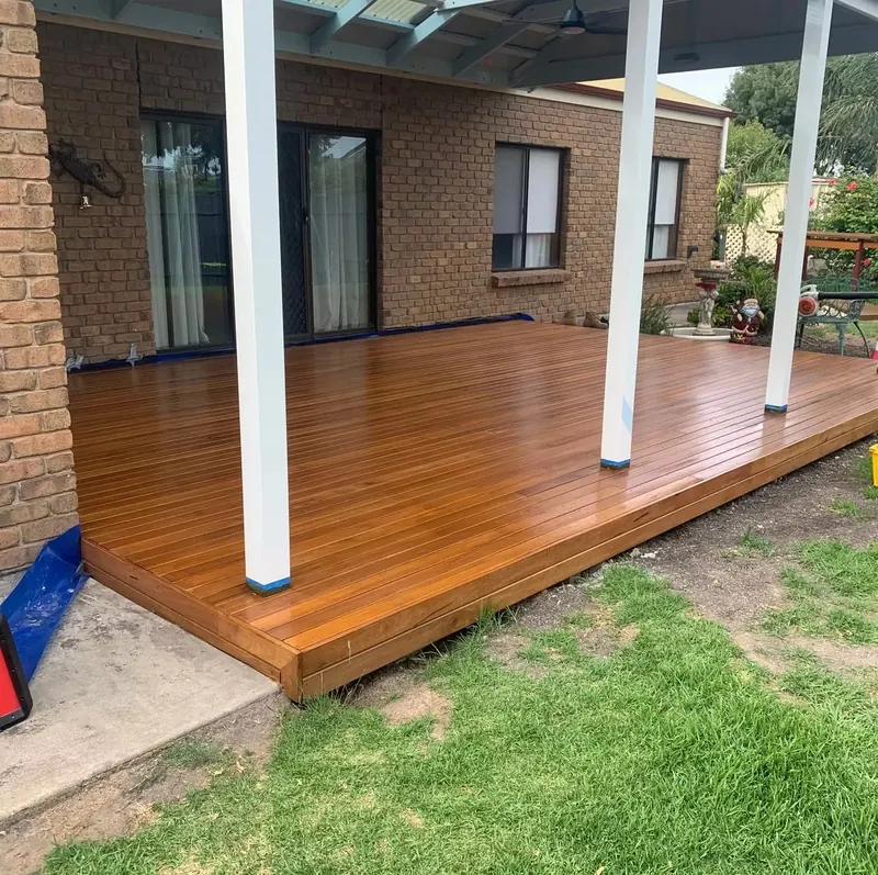 Oiled hardwood deck with white posts in a backyard beside a brick home